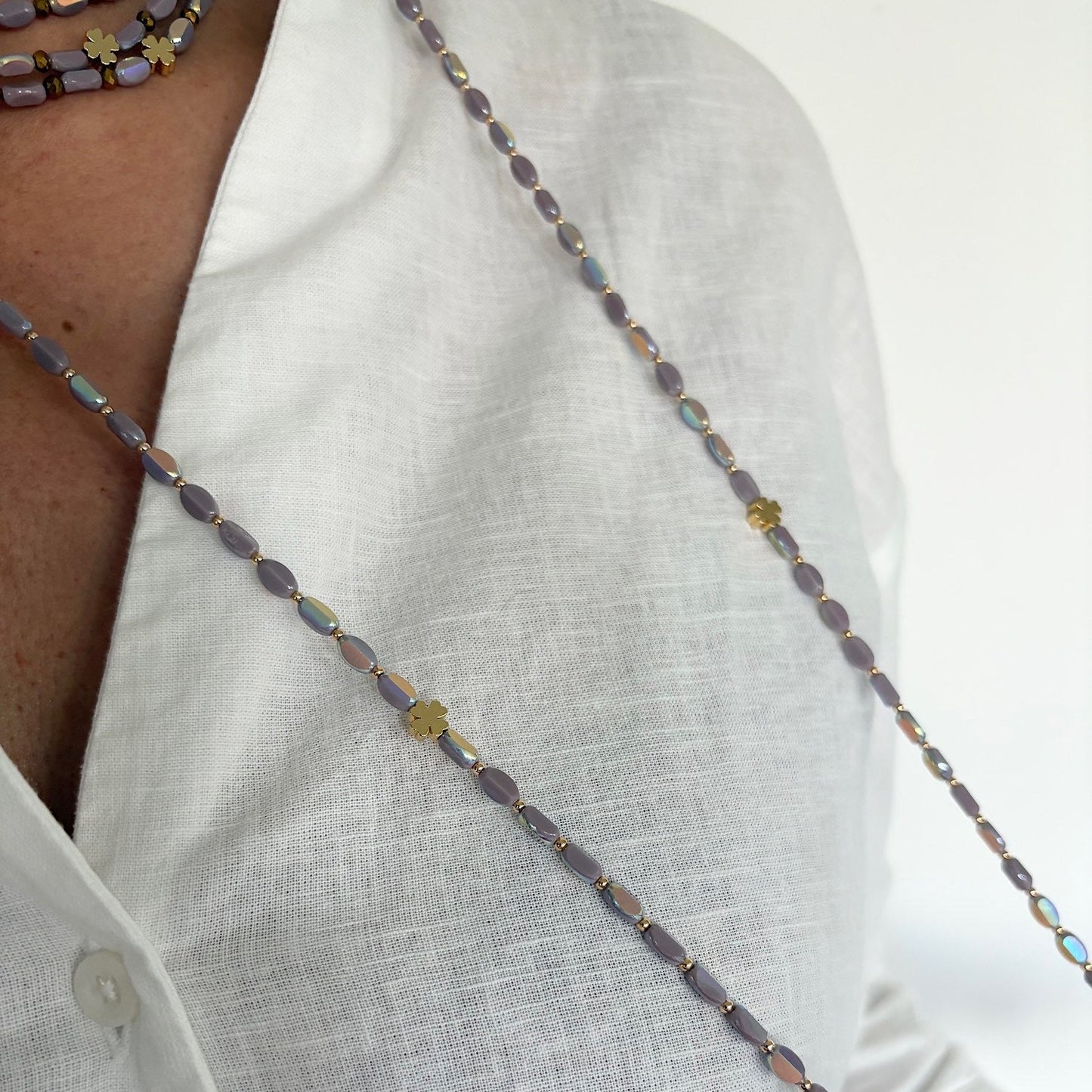 Sautoir en perles lila avec trèfles dorés porté sur chemise blanche