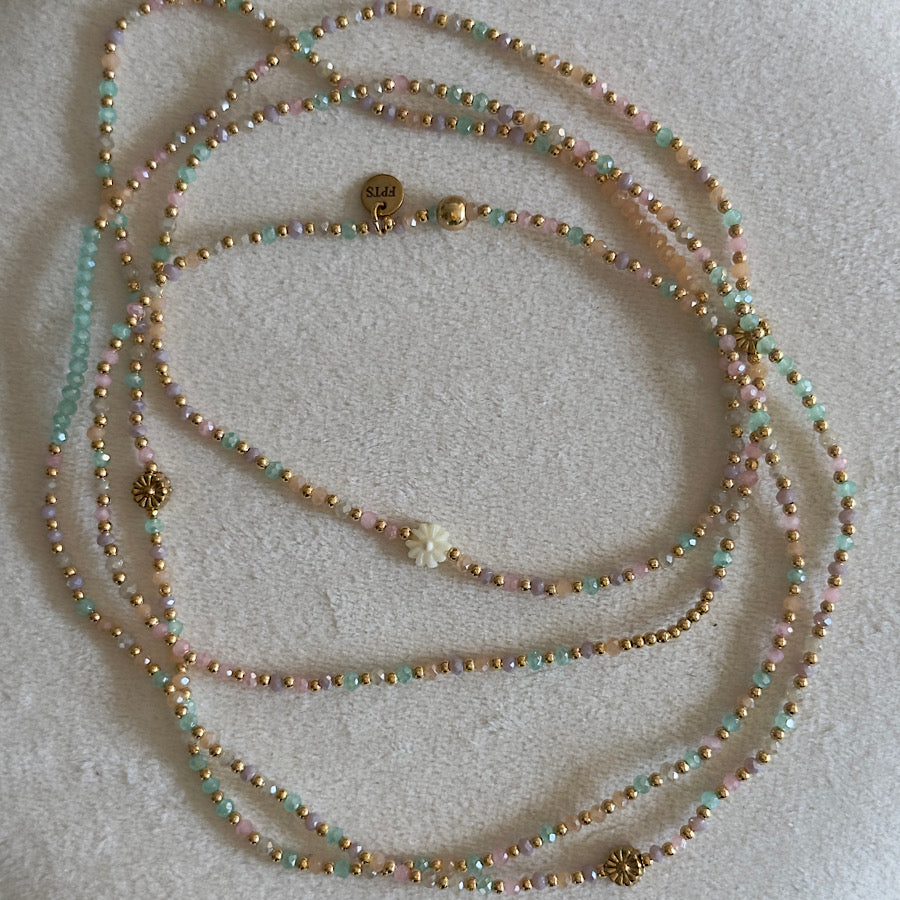Mise en valeur du sautoir Albella sous la lumière, capturant l’éclat subtil de ses perles pêche et la brillance de sa marguerite dorée.