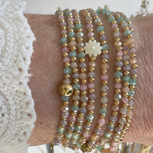 Le sautoir Albella porté en un tour, mettant en valeur ses perles de verre ultra-fines aux nuances pêche et sa marguerite dorée en coquillage.