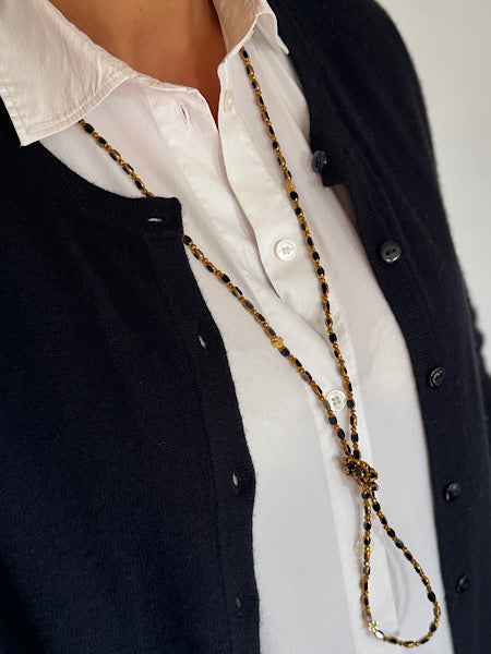 Sautoir Ébène Solaire Trèfles Dorés porté en sautoir long sur chemise blanche et gilet noir.