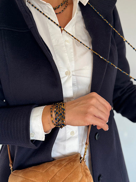 Sautoir Minuit Solaire Trèfles Dorés porté long sur chemise blanche et gilet noir – bijou en perles ovales bleues et trèfles dorés.