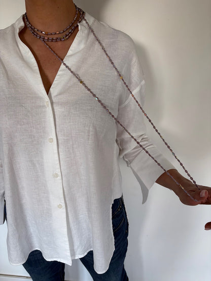 Sautoir long en perles lila avec trèfles dorés porté sur chemise