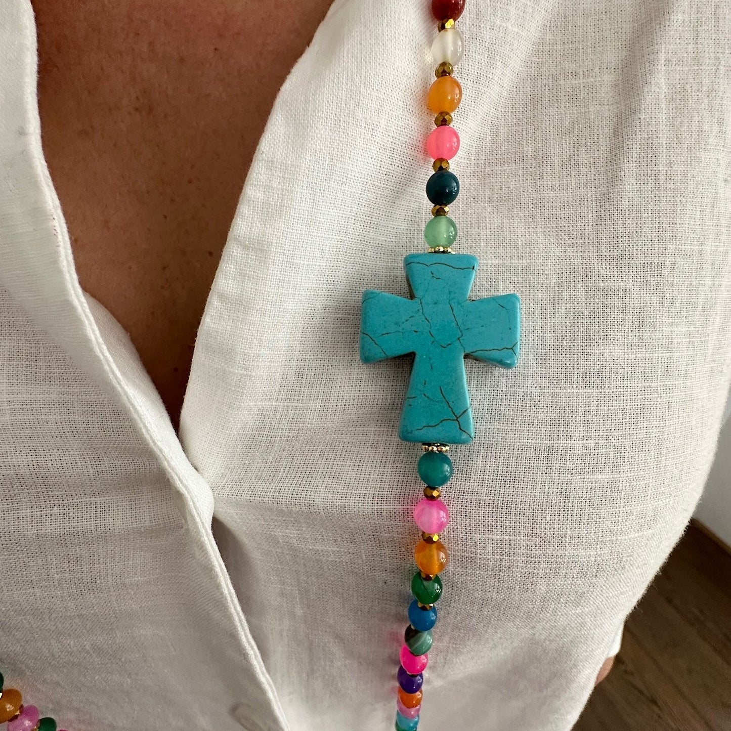 Détail croix turquoise du sautoir Colette multicolore en agate naturelle porté sur blouse blanche, bijou fait main