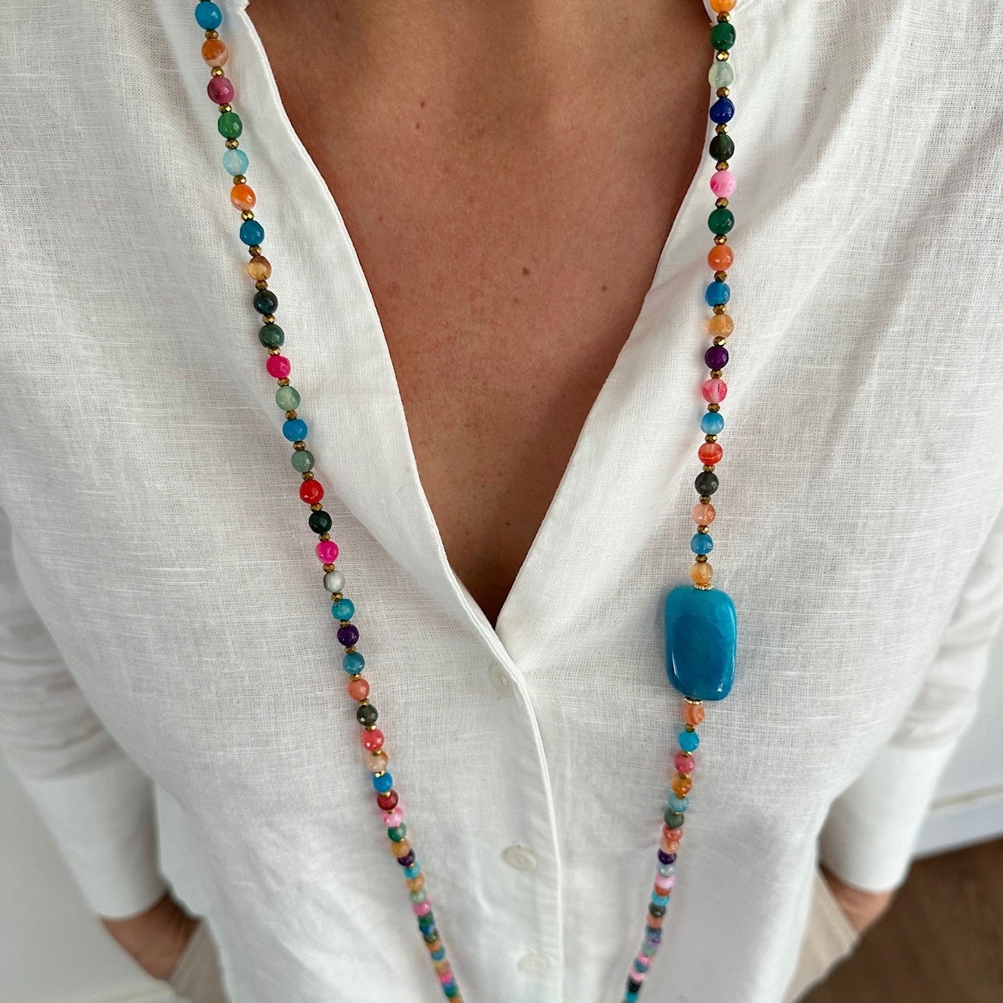Sautoir Colette en agate multicolore avec pierre bleue rectangulaire porté sur blouse blanche, bijou modulable