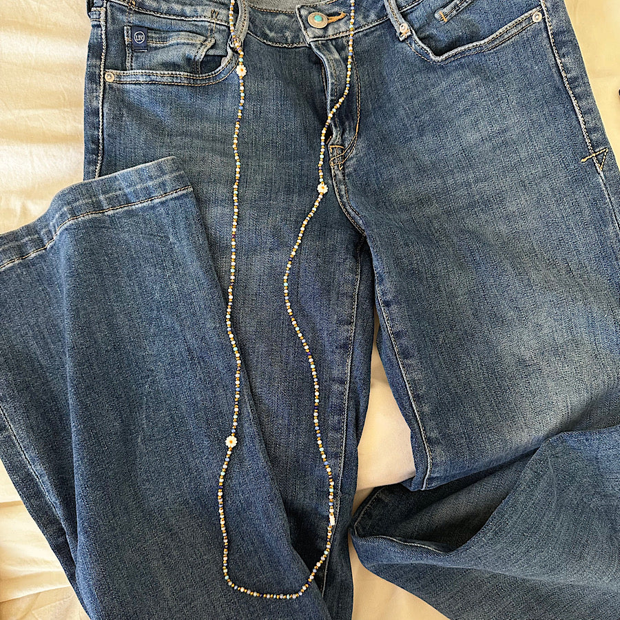 Collier sautoir perles bleues et dorées porté sur un jean
