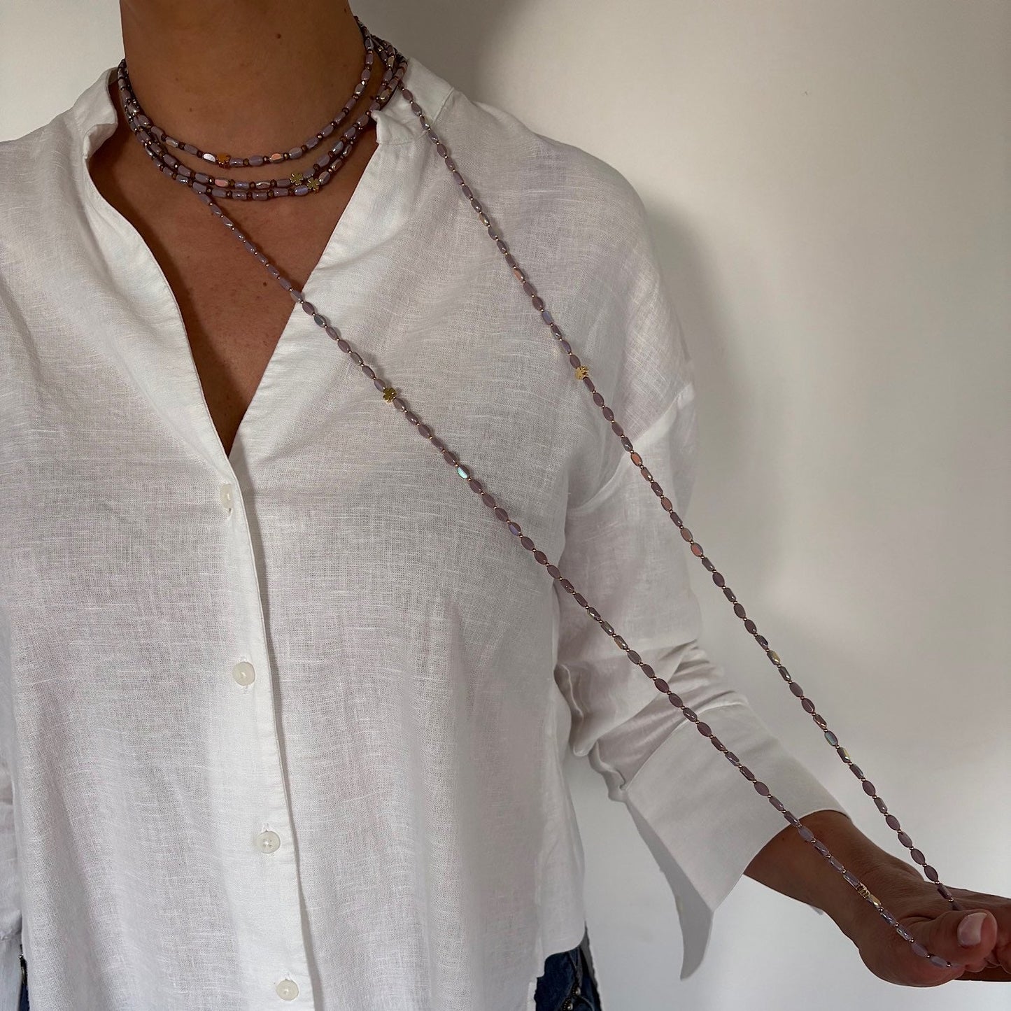Sautoir long en perles lila avec trèfles dorés porté sur chemise