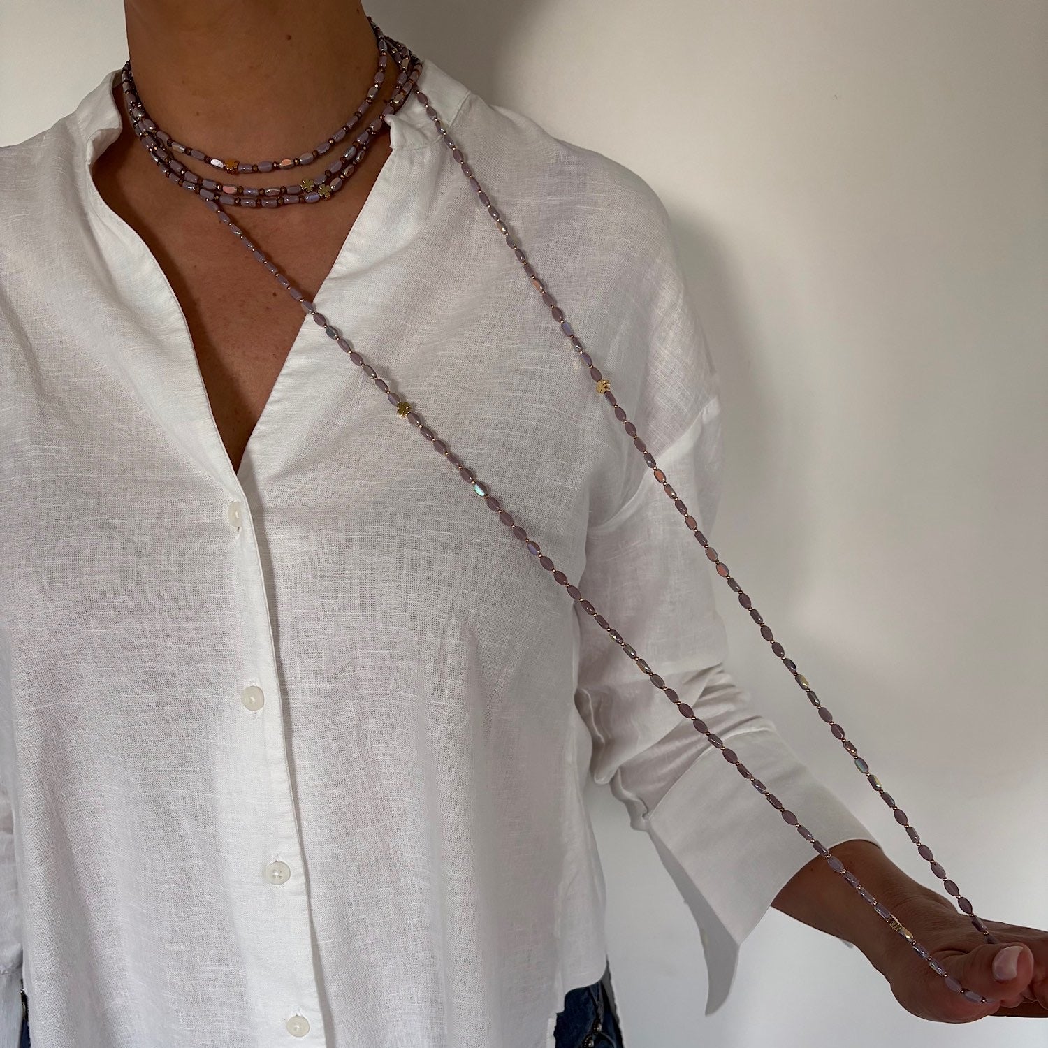 Sautoir long en perles lila avec trèfles dorés porté sur chemise