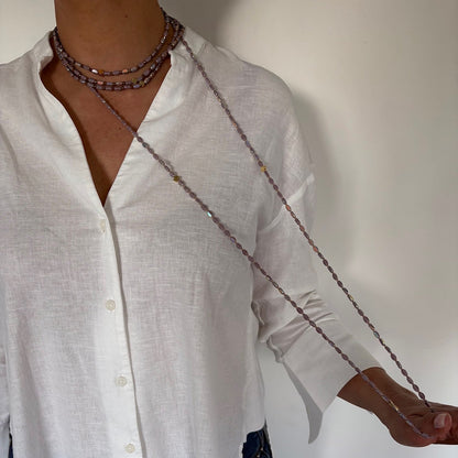 Sautoir long en perles lila avec trèfles dorés porté sur chemise