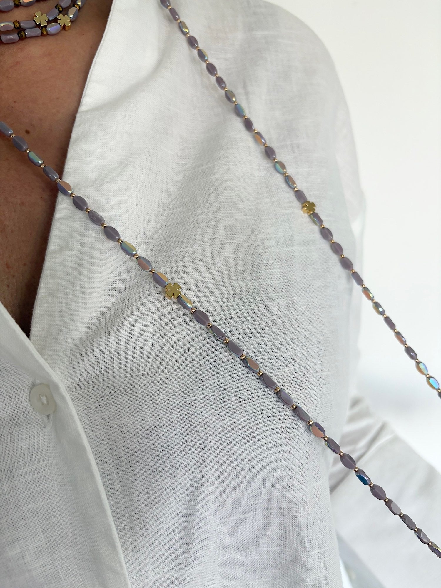 Sautoir en perles lila avec trèfles dorés porté sur chemise blanche