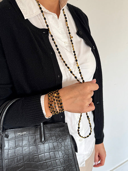 Look complet avec le sautoir Ébène Solaire Trèfles Dorés porté en manchette et sautoir, assorti à un sac noir chic.