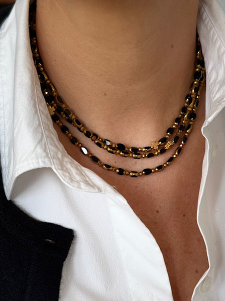 Collier Ébène Solaire Trèfles Dorés porté en ras de cou sur chemise blanche.