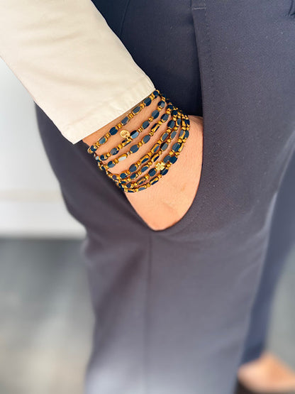 Manchette sautoir Minuit Trèfles Dorés, perles ovales bleues et dorées, porté sur pantalon marine et chemise claire.