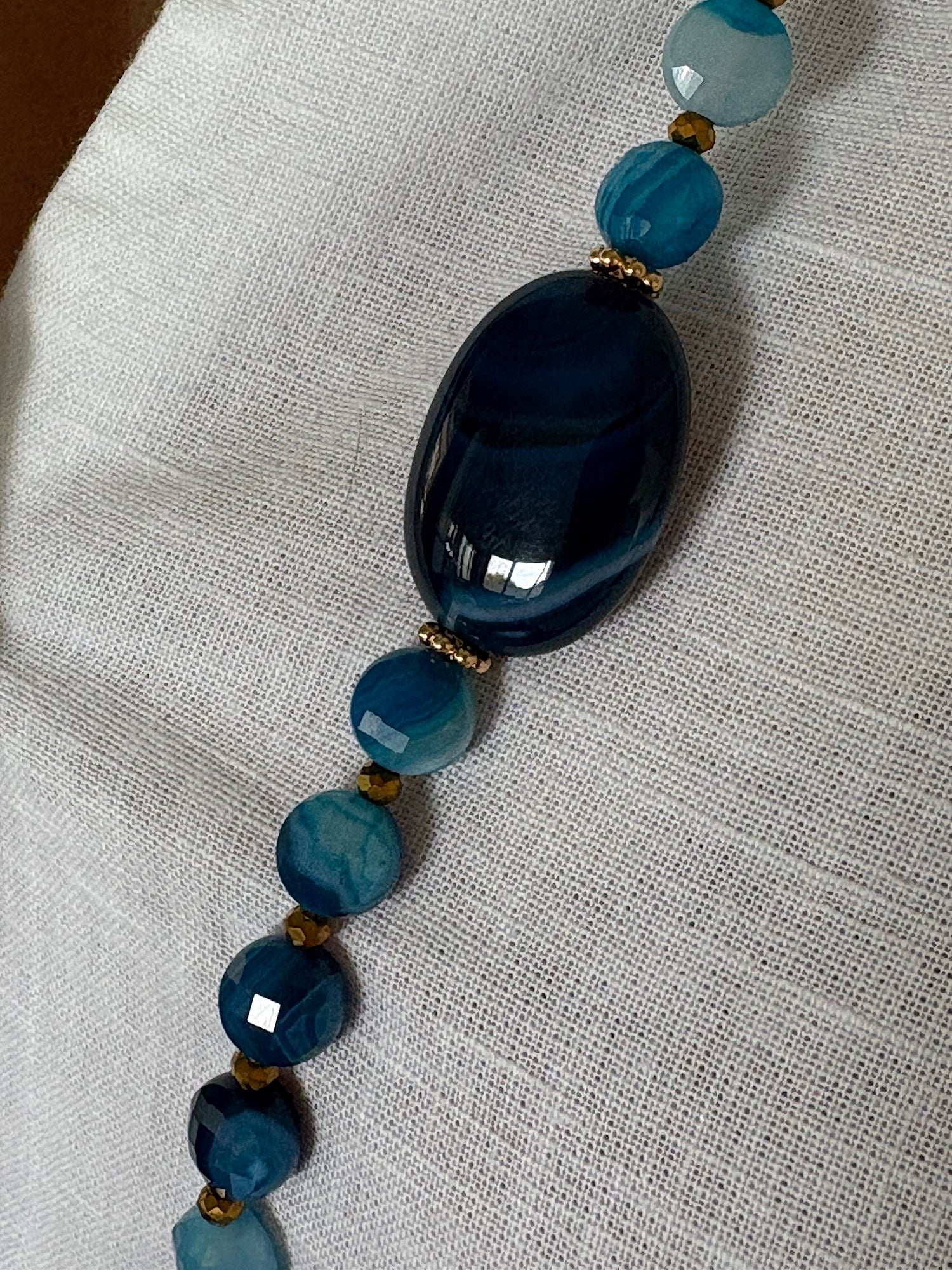 Détail du sautoir Timothée bleu avec pierre centrale en agate et perles plates, zoom sur la matière du bijou